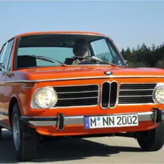 Ein leuchtend orangefarbener BMW 2002, ein Kultauto der 70er Jahre, fährt auf einer Landstraße.
