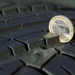 Ein 1-Euro-Stück ragt aus dem Profil eines abgefahrenen Reifens. Das zeigt, dass abgefahrene Reifen eine Strafe nach sich ziehen können.