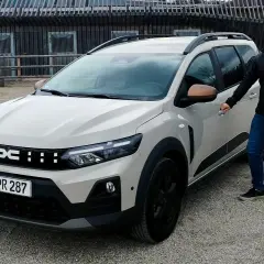 Mann neben hellem Dacia Kombi, bereit für Abenteuer. Dacia Nutzfahrzeuge – robust und vielseitig.
