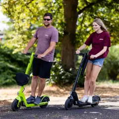 Ein Mann und eine Frau fahren nebeneinander auf E-Scootern. Sie sind im Park unterwegs, ein Ausflug mit dem e-scooter zu zweit mit kind.