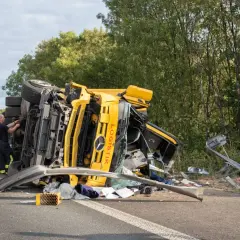 Umgekippter gelber LKW nach Unfall auf der A57. Feuerwehrleute sichern die Unfallstelle.