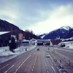 Winterliche Fahrt zum Arlbergpass. Ein Wohnwagen parkt neben der Straße, während Autos in den Tunnel fahren.