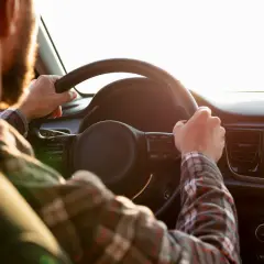 Mann mit Bart fährt Auto, Hände am Lenkrad. Er möchte sein Fahrverbot umwandeln und genießt die Fahrt.