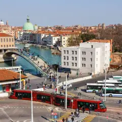 Roter Zug und Busse am Bahnhof von Venedig. Menschen überqueren eine Brücke über den Kanal.