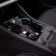 Autoinnenraum mit Gangwahlhebel, Getränkehaltern und Drehreglern. Ein Wandler ist hier nicht direkt sichtbar, aber die Bedienelemente deuten auf ein modernes Fahrzeug hin.