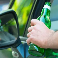 Hand hält Bierflasche im Auto. Spiegel zeigt Reflexion. Achtung: Promillegrenze Griechenland beachten!