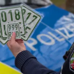 Polizeibeamter hält mehrere Kennzeichen, darunter ein kleines blaues Kennzeichen mit der Nummer 999 RHD.