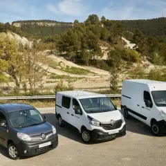 Drei Renault Kastenwagen Modelle: Kangoo, Trafic und Master, stehen nebeneinander vor einer hügeligen, bewaldeten Landschaft.