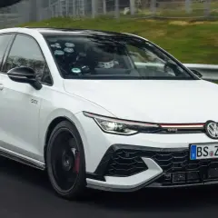 Weißer Golf GTI auf Rennstrecke, der Fahrer im Helm deutet auf den schnellsten Golf der Welt.