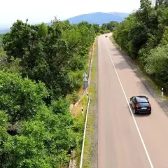 Autofahren in Kroatien auf einer kurvigen Straße durch üppige grüne Wälder, mit einem schwarzen Auto, das bergauf fährt.