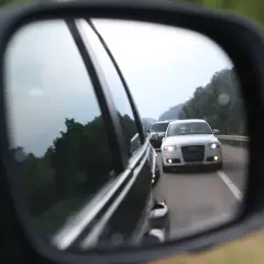 Rückspiegel zeigt weiße Audi-Limousine auf der Autobahn, die Lichthupe gibt.