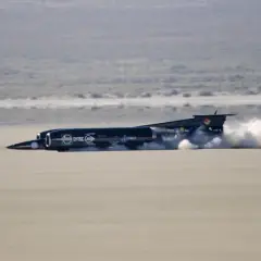 Schwarzes Raketenauto, das mit enormem Schub über eine trockene Ebene rast und eine Staubwolke hinterlässt. Der Thrust SSC ist ein Meisterwerk der Ingenieurskunst.