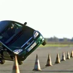 Ein grüner Kleinwagen kippt im Elchtest gefährlich zur Seite, während er eine Reihe von Pylonen umfährt.