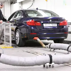 Blauer BMW auf einem Prüfstand, Abgasrohr angeschlossen für Euro 6c Tests. Ein Techniker überwacht die Messungen.