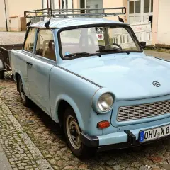 Hellblauer Trabant mit Anhänger auf Kopfsteinpflaster. Ein Auto gilt ab 30 Jahren als Oldtimer.