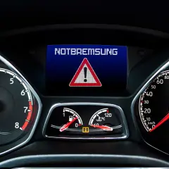 Armaturenbrett zeigt "NOTBREMSUNG" an. Assistenzsysteme im Auto sind Pflicht, um solche Warnungen zu vermeiden.