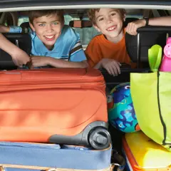 Zwei lächelnde Jungen schauen über Koffer und Taschen im Kofferraum. Die Koffer sind gepackt, die reise checkliste ist abgehakt.