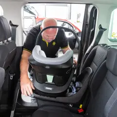 Mann montiert einen Kindersitz im Auto. Dieser Kindersitz ist ideal für Reisen, vielleicht sogar nach Italien.