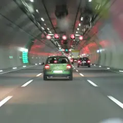 Fahrt durch einen Tunnel mit Autos. Über der Fahrbahn sind rote Verkehrsschilder mit Geschwindigkeitsbegrenzungen zu sehen, die wie ein infrarot blitzer wirken.