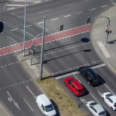 Autos warten an einer Kreuzung für mehrspuriges Abbiegen. Ein roter Kleinwagen und ein schwarzer Van sind zu sehen.