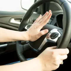 Hand drückt Hupe am Lenkrad. Darf man mit defekter Hupe fahren? Das ist eine wichtige Frage für die Verkehrssicherheit.