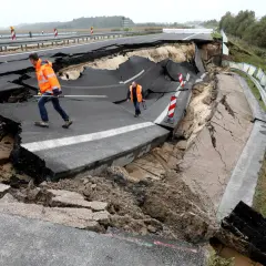 Zwei Männer in Warnwesten inspizieren eine eingestürzte Autobahn A20. Der Asphalt ist aufgebrochen und klafft tief.