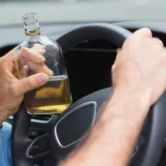 Mann hält Flasche Alkohol am Steuer. 2 Promille wieviel Alkohol? Gefährliche Fahrt.