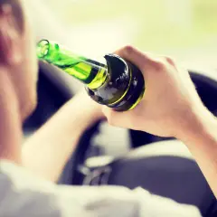 Mann hält Flasche im Auto, ignoriert die Promillegrenze beim Autofahren.