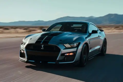 Silberner Ford Mustang Shelby GT500 mit schwarzen Streifen fährt auf einer Straße in der Wüste.
