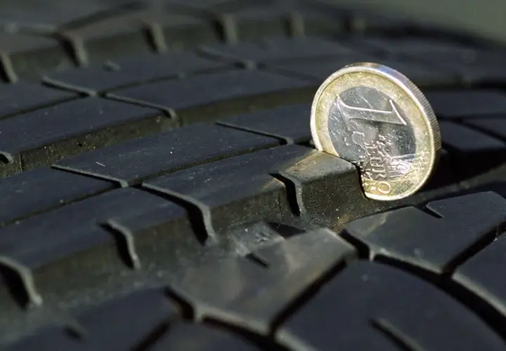 Ein 1-Euro-Stück ragt aus dem Profil eines abgefahrenen Reifens. Das zeigt, dass abgefahrene Reifen eine Strafe nach sich ziehen können.