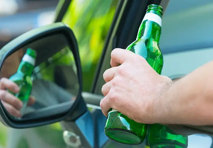 Hand hält Bierflasche im Auto. Spiegel zeigt Reflexion. Achtung: Promillegrenze Griechenland beachten!