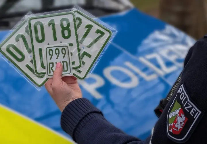 Polizeibeamter hält mehrere Kennzeichen, darunter ein kleines blaues Kennzeichen mit der Nummer 999 RHD.