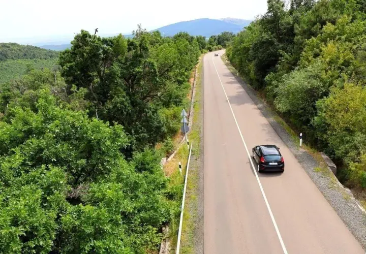 Autofahren in Kroatien auf einer kurvigen Straße durch üppige grüne Wälder, mit einem schwarzen Auto, das bergauf fährt.