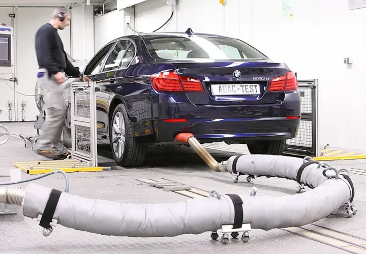 Blauer BMW auf einem Prüfstand, Abgasrohr angeschlossen für Euro 6c Tests. Ein Techniker überwacht die Messungen.