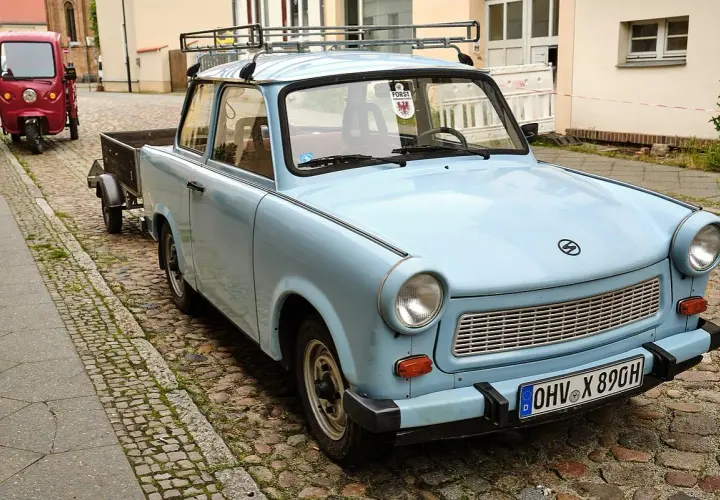 Hellblauer Trabant mit Anhänger auf Kopfsteinpflaster. Ein Auto gilt ab 30 Jahren als Oldtimer.