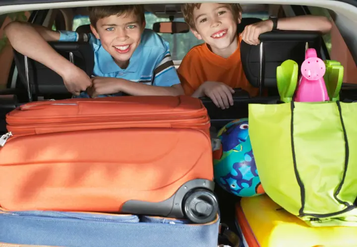 Zwei lächelnde Jungen schauen über Koffer und Taschen im Kofferraum. Die Koffer sind gepackt, die reise checkliste ist abgehakt.