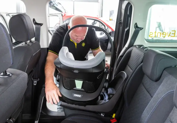 Mann montiert einen Kindersitz im Auto. Dieser Kindersitz ist ideal für Reisen, vielleicht sogar nach Italien.