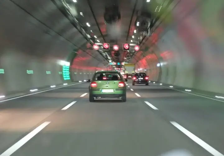 Fahrt durch einen Tunnel mit Autos. Über der Fahrbahn sind rote Verkehrsschilder mit Geschwindigkeitsbegrenzungen zu sehen, die wie ein infrarot blitzer wirken.