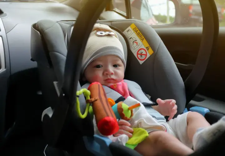 Ein Baby im Kindersitz vorne im Auto. Die Frage "ab wann darf ein Kind vorne sitzen" ist hier relevant, da es auf die richtige Sicherung ankommt.