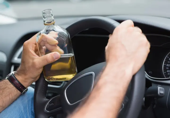 Mann hält Flasche Alkohol am Steuer. 2 Promille wieviel Alkohol? Gefährliche Fahrt.