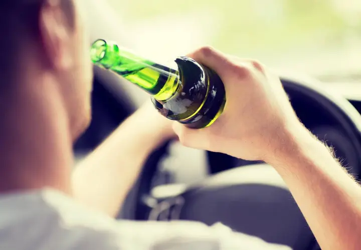Mann hält Flasche im Auto, ignoriert die Promillegrenze beim Autofahren.
