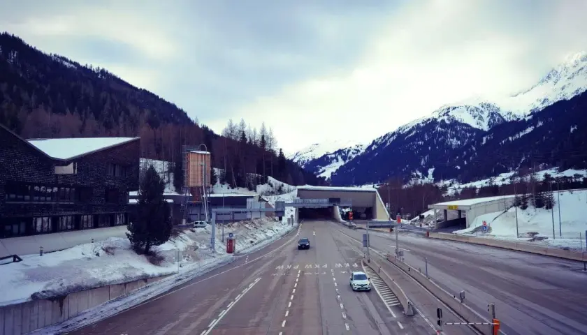 Winterliche Fahrt zum Arlbergpass. Ein Wohnwagen parkt neben der Straße, während Autos in den Tunnel fahren.