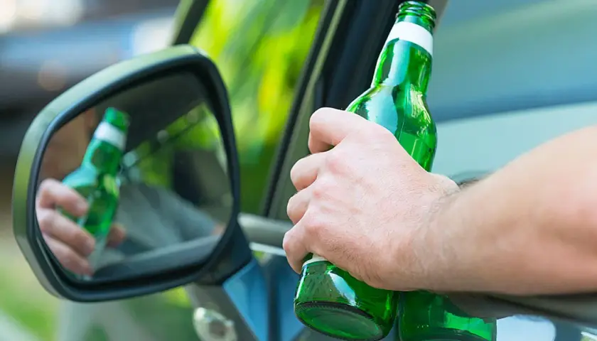 Hand hält Bierflasche im Auto. Spiegel zeigt Reflexion. Achtung: Promillegrenze Griechenland beachten!