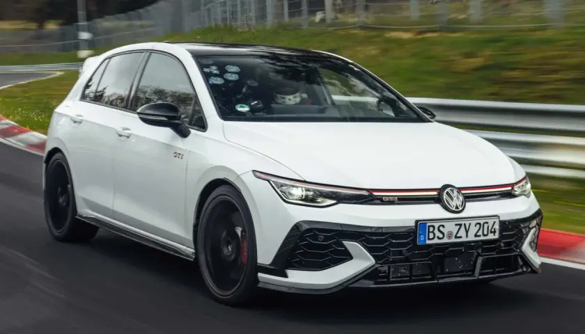 Weißer Golf GTI auf Rennstrecke, der Fahrer im Helm deutet auf den schnellsten Golf der Welt.