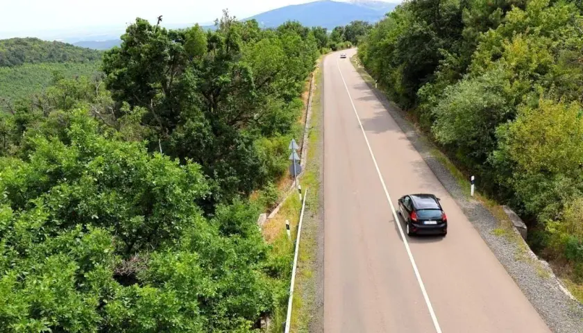 Autofahren in Kroatien auf einer kurvigen Straße durch üppige grüne Wälder, mit einem schwarzen Auto, das bergauf fährt.