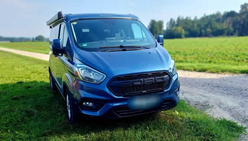 Blauer Campervan (Westfalia) steht auf einer Wiese neben einem Feldweg. Hoffentlich keine uebler i21 probleme auf der Reise!