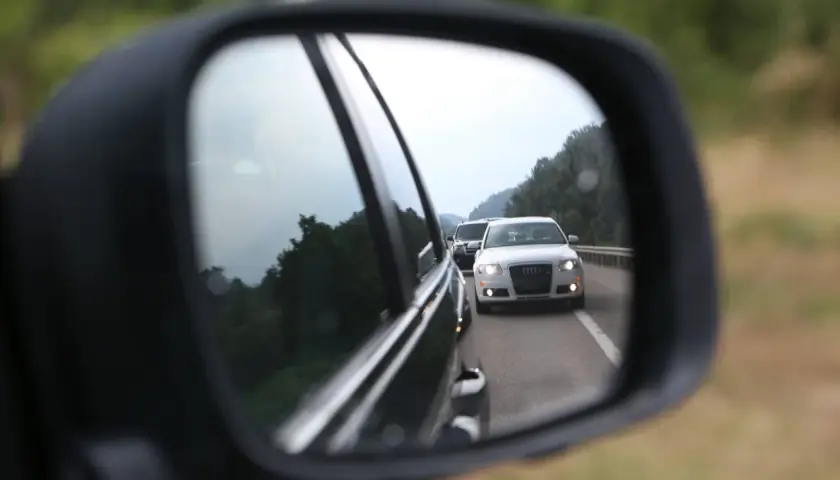 Rückspiegel zeigt weiße Audi-Limousine auf der Autobahn, die Lichthupe gibt.
