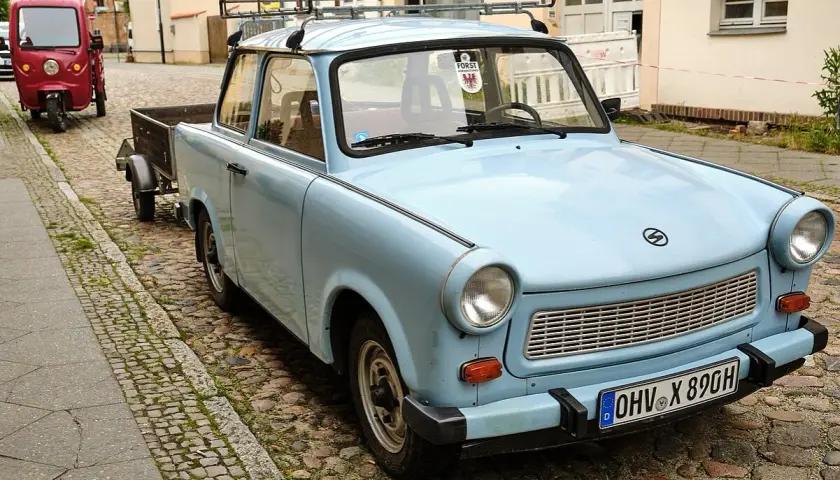 Hellblauer Trabant mit Anhänger auf Kopfsteinpflaster. Ein Auto gilt ab 30 Jahren als Oldtimer.