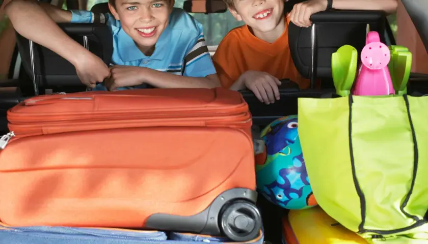 Zwei lächelnde Jungen schauen über Koffer und Taschen im Kofferraum. Die Koffer sind gepackt, die reise checkliste ist abgehakt.