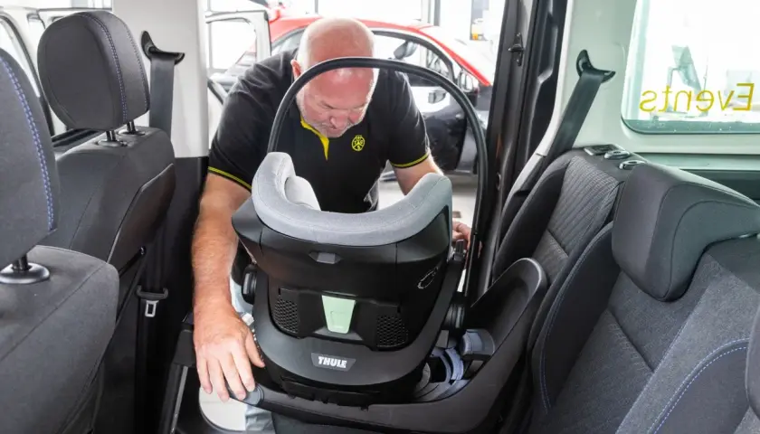 Mann montiert einen Kindersitz im Auto. Dieser Kindersitz ist ideal für Reisen, vielleicht sogar nach Italien.